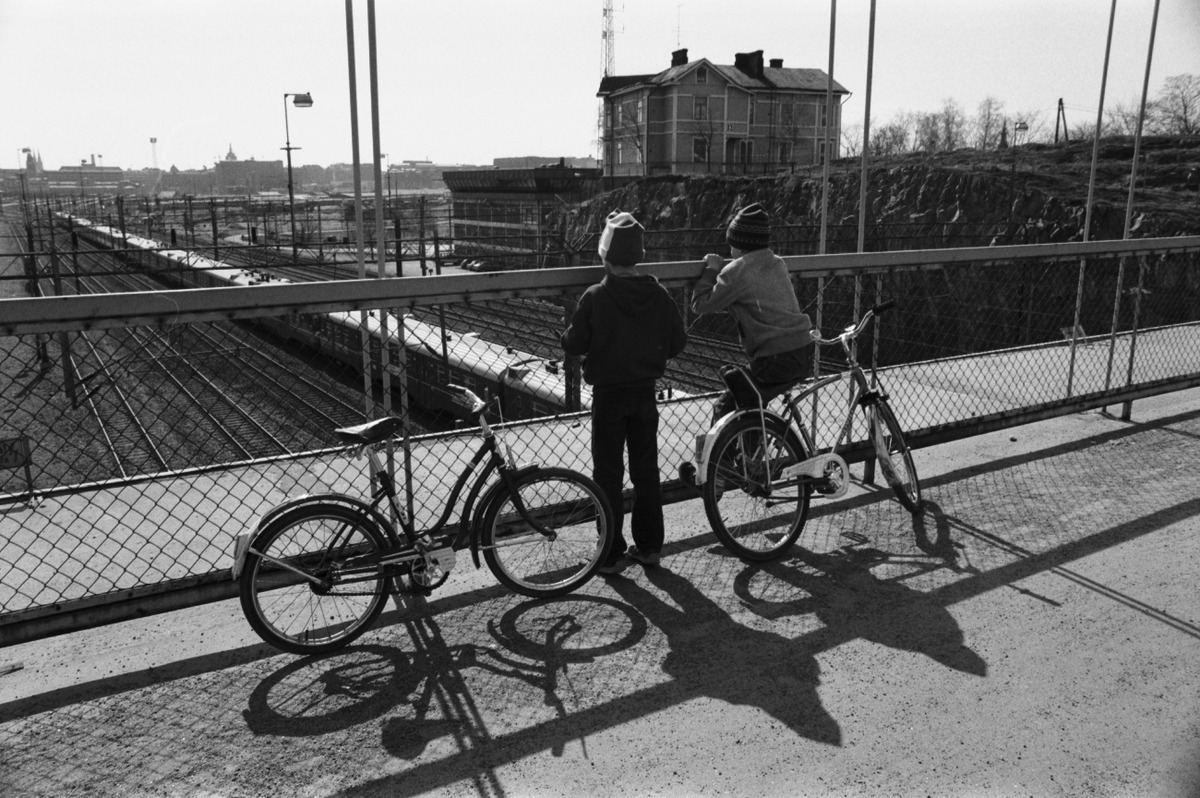 Kaksi poikaa (Tuomas Heikkilä ja Aapo Rista) polkupyörineen katselemassa junien kulkua Linnunlaulun sillalla
