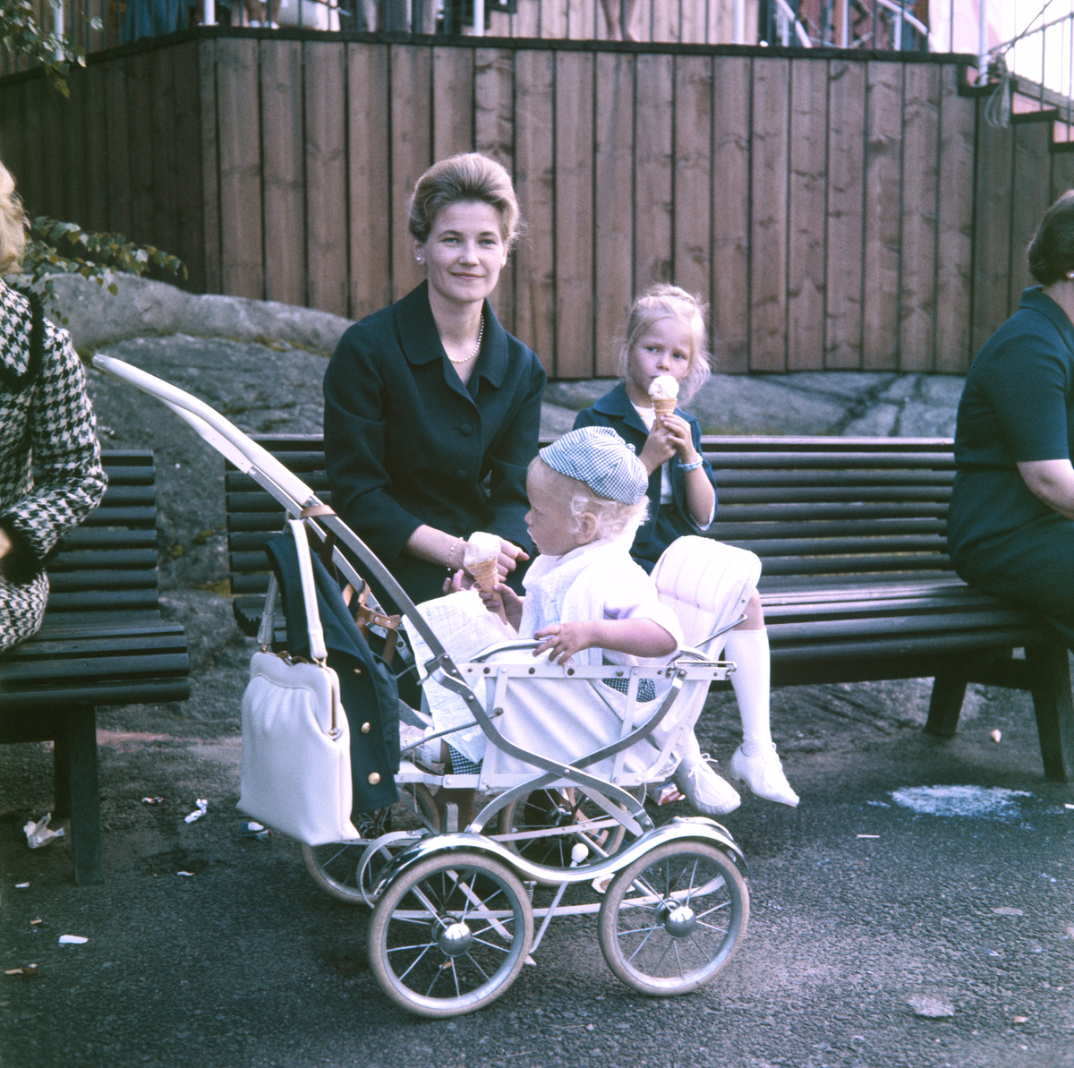 Äiti istuu lasten kanssa penkillä Linnanmäellä