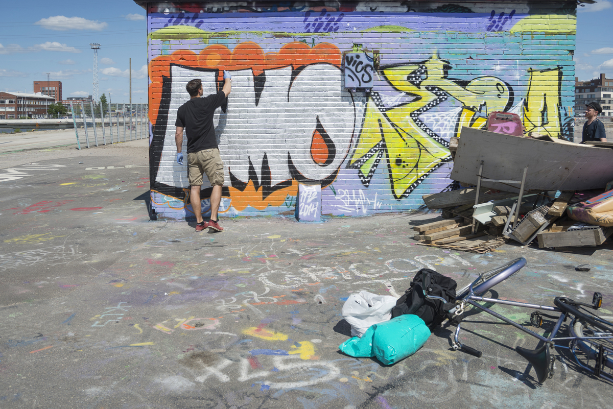 Graffititaiteilija työssään Kalasatamassa Suvilahden kaasukellon ja Junatien liittymän tuntumassa