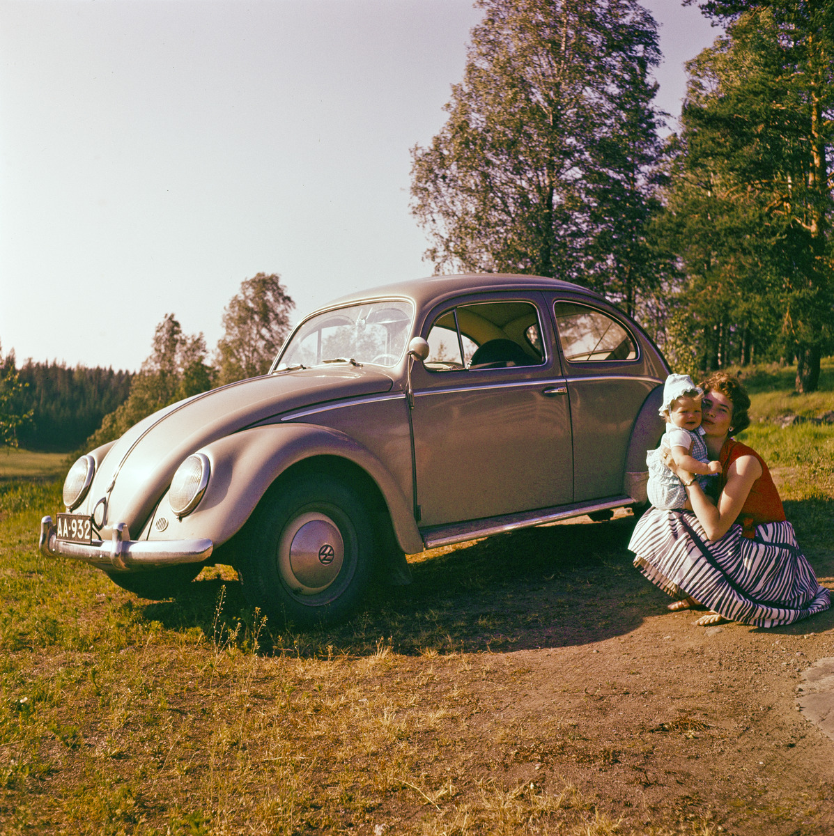 Nainen lapsen kanssa luonnossa vierellään Volkswagen Kupla (typ 1)