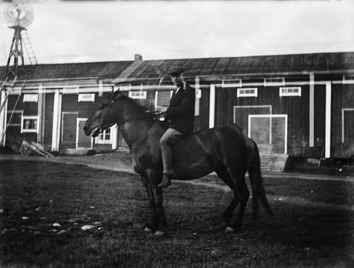 Mies satuloimattoman hevosen selässä varastorakennuksen luona