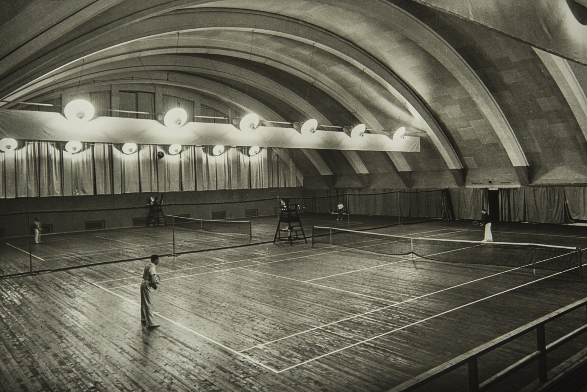 Miehiä pelaamassa tennistä asianmukaisissa tennisasuissaan Helsingin tennishallissa