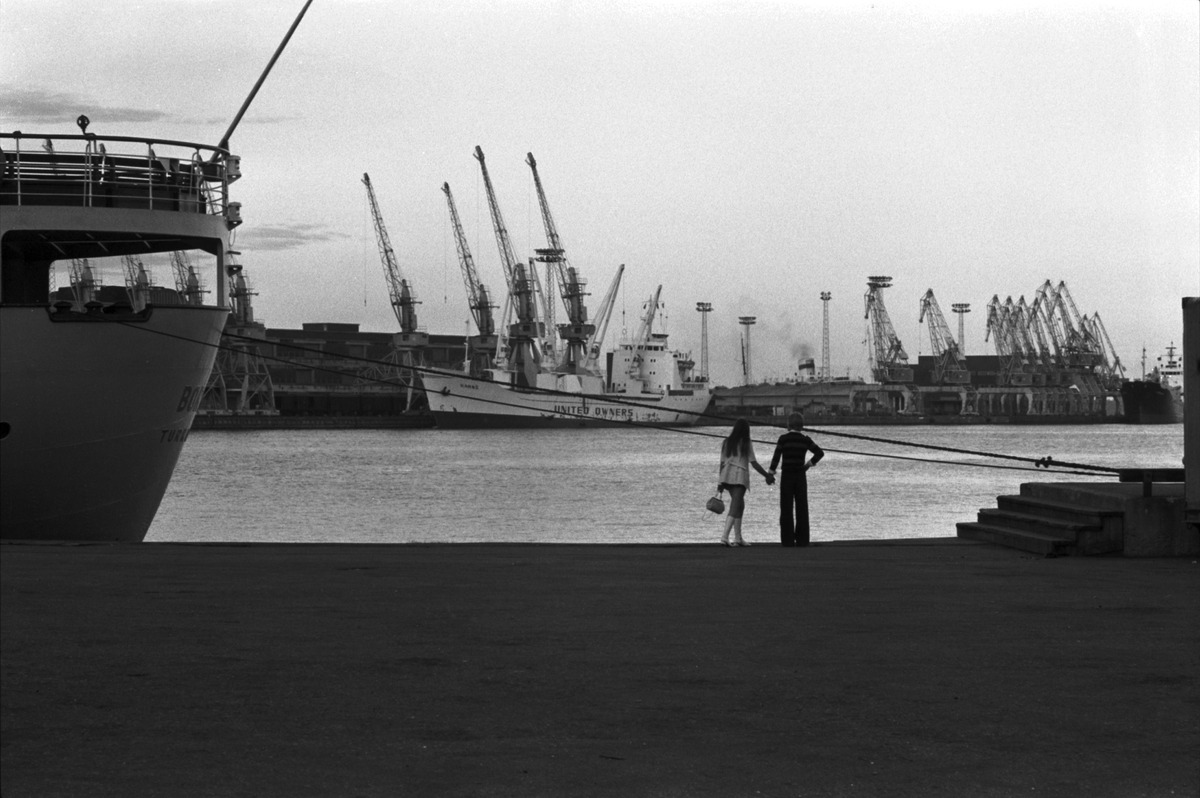 Käsi kädessä laiturilla seisovat nuori nainen ja mies katselemassa merelle Eteläsatamassa