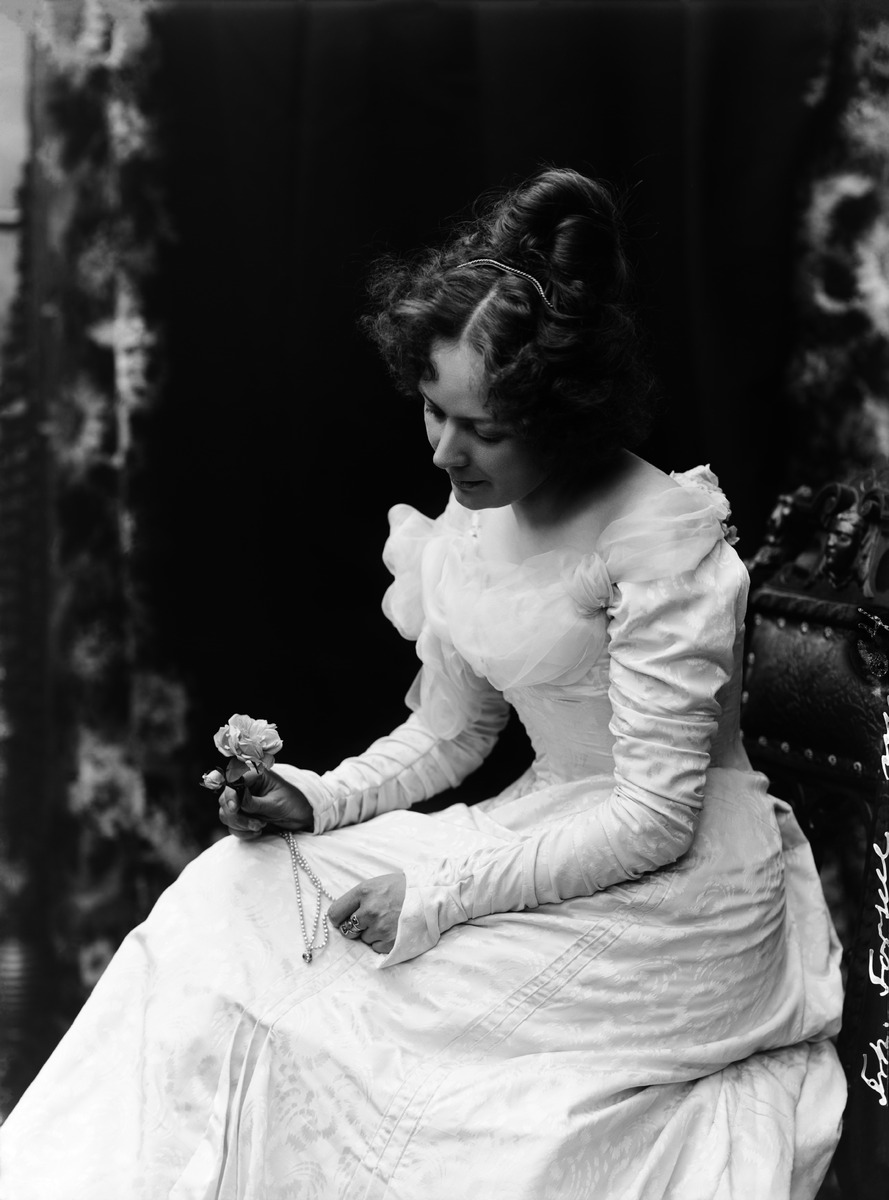 Laulaja Elli Forsell (1873–1943) istumassa tuolilla käsissään kaulariipus ja ruusu